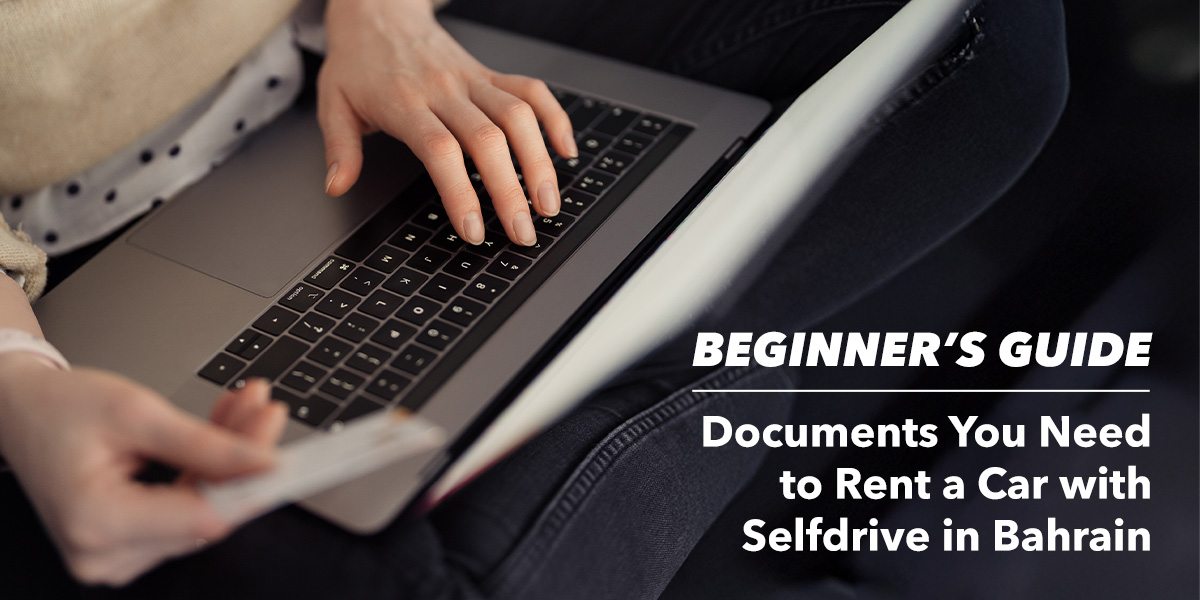 A person is sitting with a laptop, typing with one hand and holding a document. Text overlay reads, "Beginner's Guide: Documents You Need to Rent a Car with Selfdrive in Bahrain."